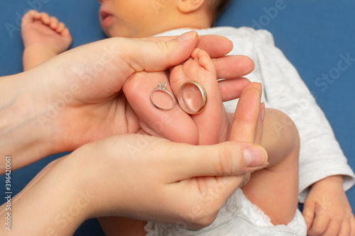 Closeup of newborn baby's foot with wedding rings together. Mother holding baby's foot. Happy Family concept. Beautiful maternity photo. 