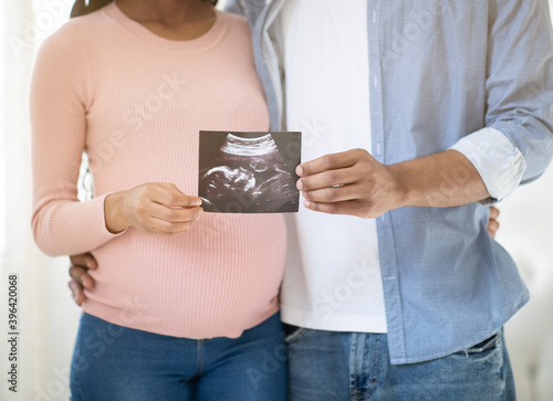 Cropped view of young pregnant couple holding photo of their unborn baby indoors, close up