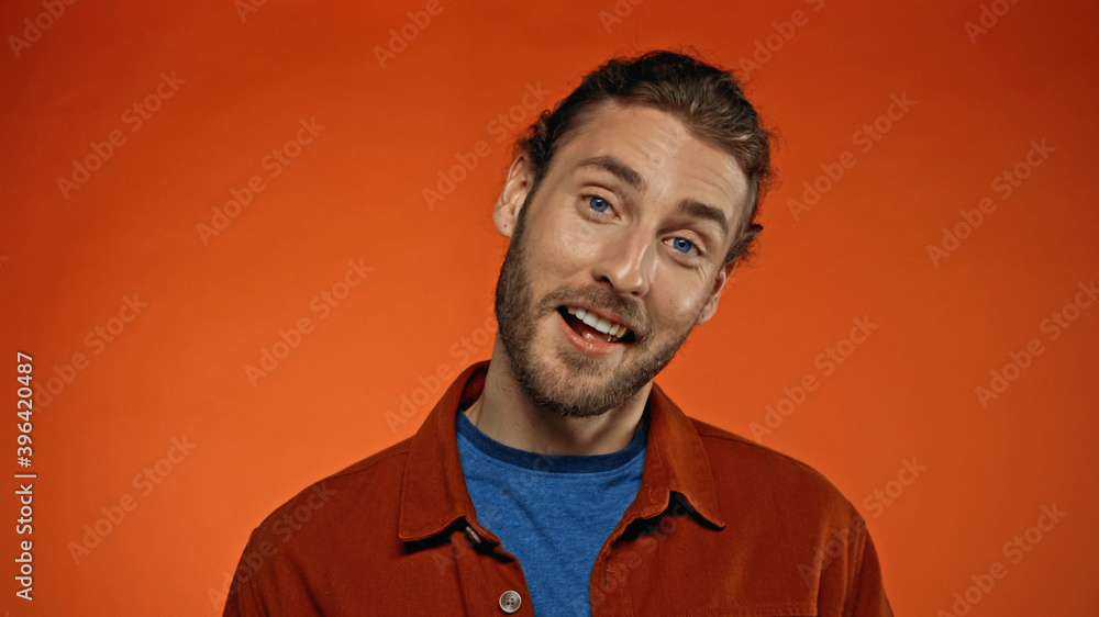 happy and bearded man smiling while looking at camera on orange happy and bearded man smiling while looking at camera on orange