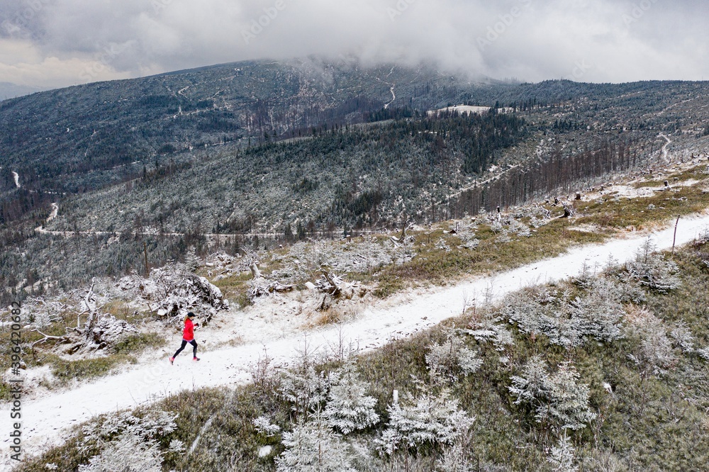 Aerial view on a running girl in a red sweatshirt on a mountain trail.