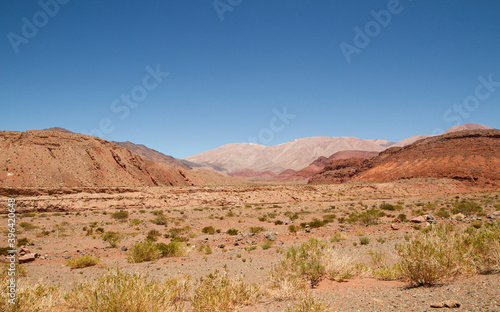 Desert landscape. View of the arid valley, red sand, sandstone formations and mountains under a deep blue sky.