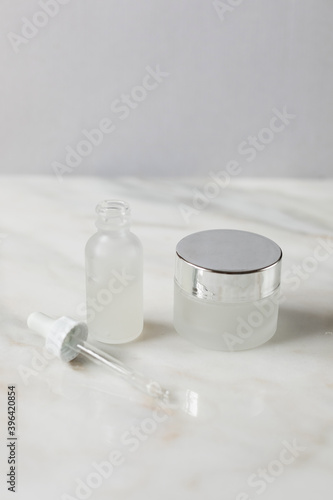 frosted white dropper bottle and frosted white cream bottle on marble surface, beauty products, skincare 