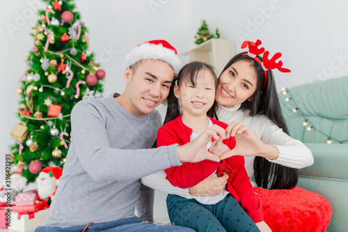 Asian family show heart sign with hands, they party near Christmas tree, they feeling happy and smiling, they rest on floor, child development and family activity, celebration in Christmas season