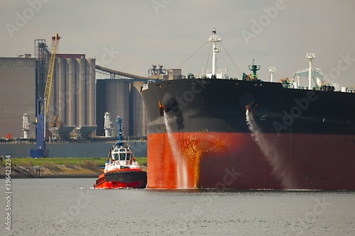 Large crude oil tanker ship pumping out ballast water when coming into port in Rotterdam, tug boat pushing the side photo