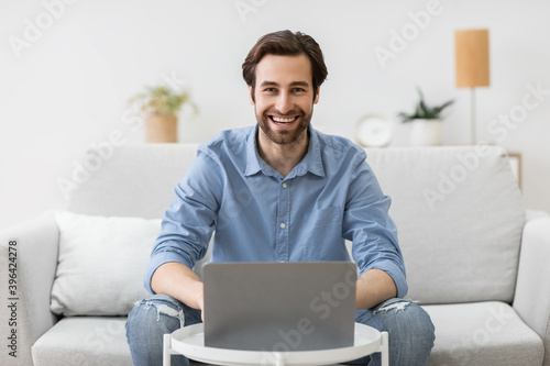 Man at laptop computer works online and smiles at home