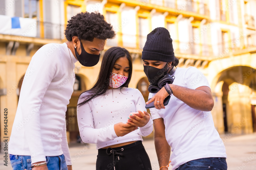 Lifestyle, Latino friends having fun with face masks looking at something on the phone. Friendships in the coronavirus pandemic, covid-19. Social distance, social responsibility, new normal