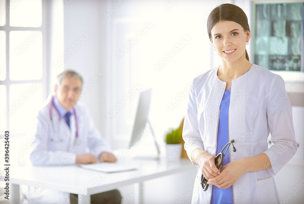 A doctor looking at the camera with her male colleage in the back of the conference room in hospital A doctor looking at the camera with her male colleage in the back of the conference room in hospital