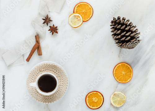 Christmas frame with a cup of coffee, ribbons, dried oranges, pine cones, anise stars and cinnamon on marble background with copy space. Flat lay, light, orange