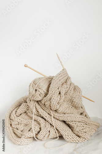 knitting: wooden knitting needles and beige wool yarn tucked into beige woven blanket against white wall on marble top 