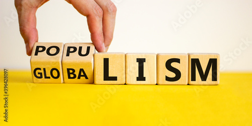 Populism or globalism. Hand turns cubes and changes word 'globalism' to 'populism'. Beautiful yellow table, white background, copy space. Business and populism or globalism concept. photo