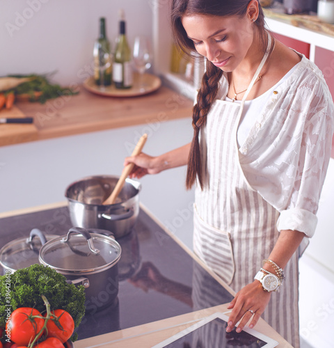 Young woman using a tablet computer to cook in her kitchen