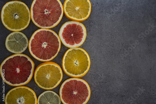 Fototapeta Naklejka Na Ścianę i Meble -  Fruit frame or border. Fresh juicy orange, lemon and grapefruit slices on a table. Dark gray background with copy space. Healthy eating concept.  