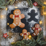 gingerbread men.
Three ginger men, one big, two small. Against the backdrop of snow made of flour, fir branches and a wooden background. Homemade cookies, Christmas baked goods. December traditions