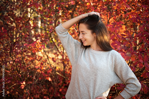 A very happy young girl stands in the autumn forest and smiles. The foliage behind it is bright red.
