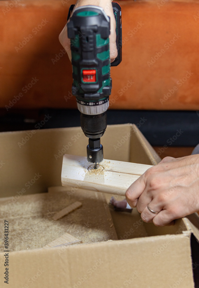  a man drills a big hole in the board on a cardboard box at home, DIY