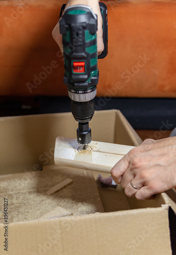  a man drills a big hole in the board on a cardboard box at home, DIY