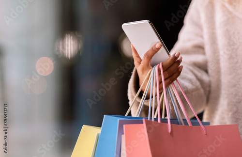 Happy black woman using smartphone, holding shopping bags