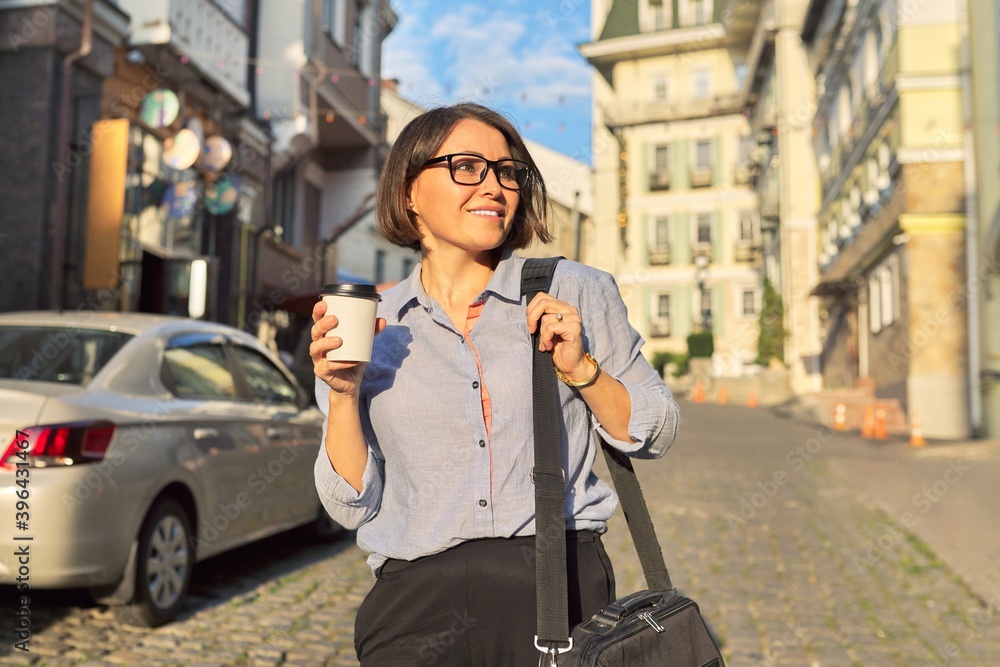 Fototapeta premium Mature business woman in glasses with office laptop bag walking along city street