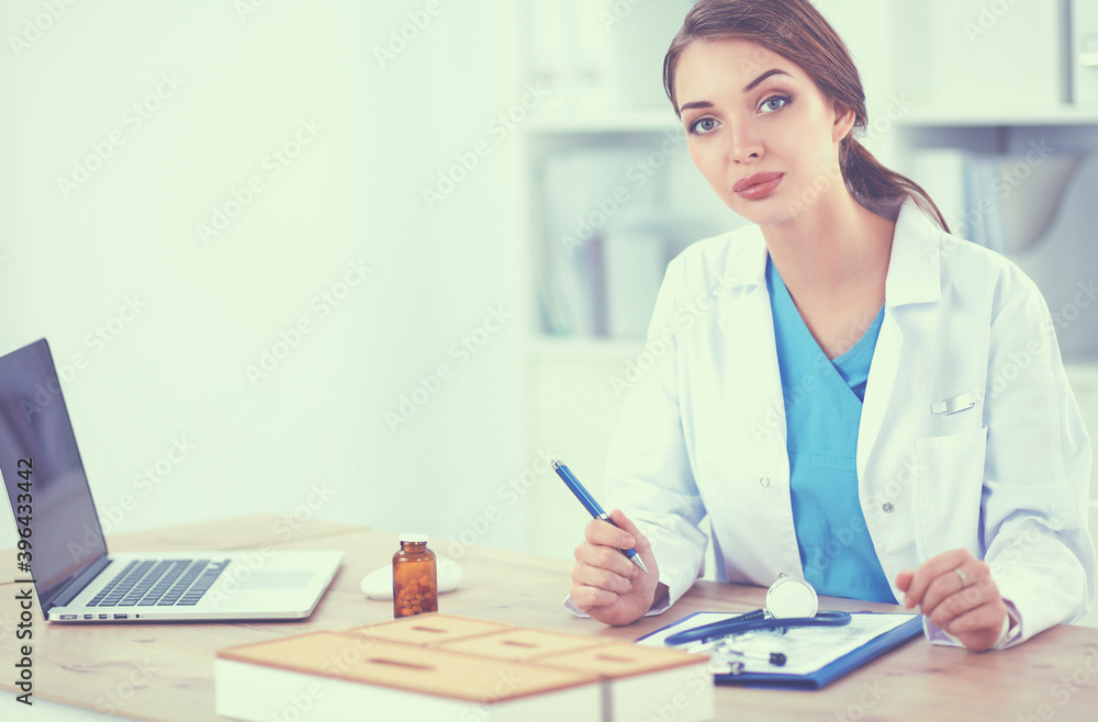 Beautiful young smiling female doctor sitting at the desk and writing. Beautiful young smiling female doctor sitting at the desk and writing.