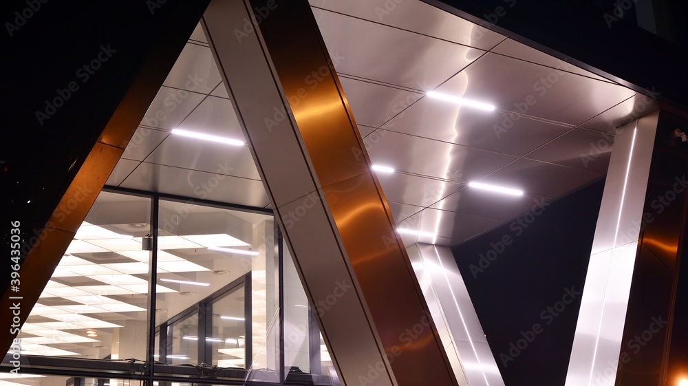 Fototapeta premium Combination of metal and glass wall material. Steel facade on columns. Abstract modern architecture. High-tech minimalist office building. Contemporary business architecture abstract fragment in night