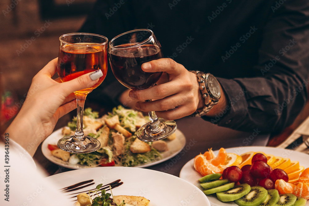 hands with glasses clinking against the background of Christmas tree lights and bonfires from a home fireplace over a table with delicious dishes hands with glasses clinking against the background of Christmas tree lights and bonfires from a home fireplace over a table with delicious dishes