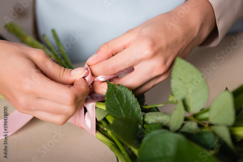 Close up view of florist hands tying stalks of bouquet with decorative ribbon on blurred background