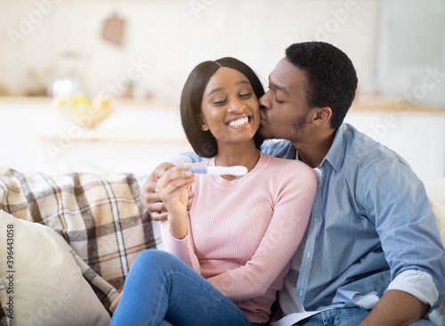 Caring black husband kissing his lovely young wife on cheek, happy to learn about her pregnancy from test, copy space