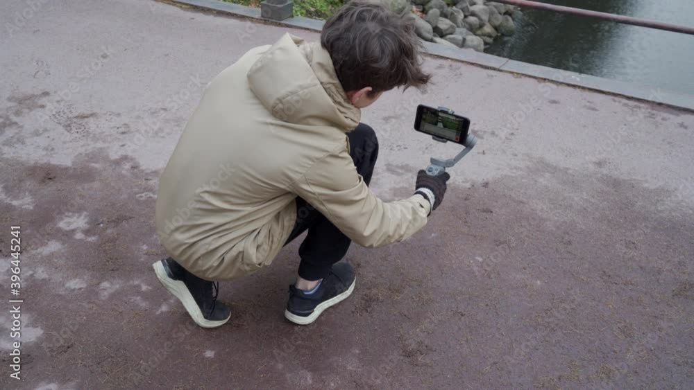 Teenage boy shooting video using mobile phone gimbal stabilizer in autumn park. Catherine Park, Tsarskoye Selo, Saint Petersburg, Russia. Teenage boy shooting video using mobile phone gimbal stabilizer in autumn park. Catherine Park, Tsarskoye Selo, Saint Petersburg, Russia.
