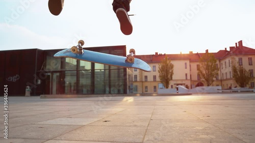SLOW MOTION TIME WARP, CLOSE UP, LOW ANGLE, LENS FLARE, DOF: Unrecognizable skater does a flip trick while riding around a square. Cinematic shot of a skateboarder doing a nollie kickflip at sunset.