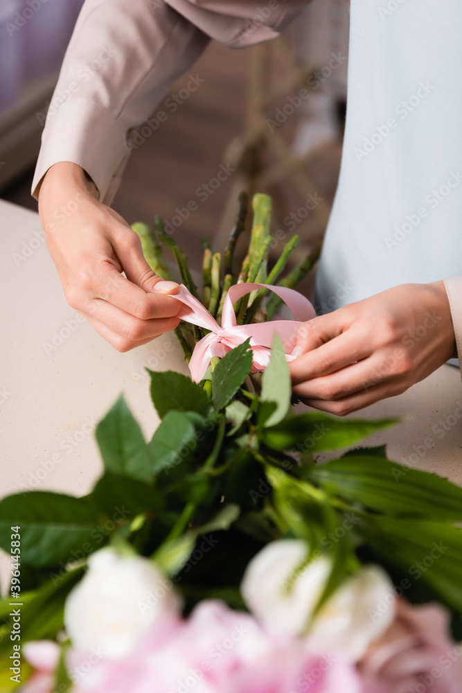 Cropped view of florist tying bow on bouquet stalks on blurred foreground