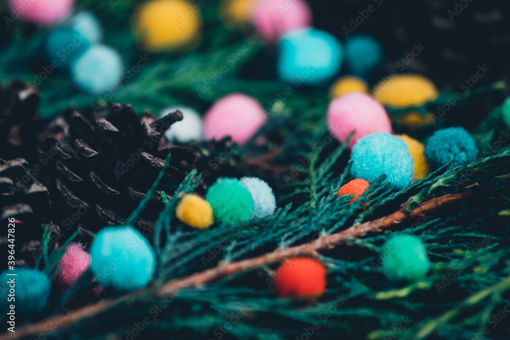 Closeup view of evergreen trees mixed branches and pinecones with small colorful pompoms, slightly alternative christmas setup approach, soft varied pompoms placed on christmas tree branches Closeup view of evergreen trees mixed branches and pinecones with small colorful pompoms, slightly alternative christmas setup approach, soft varied pompoms placed on christmas tree branches