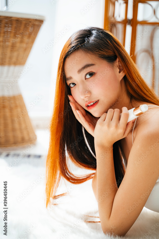Naklejka premium Side view of asian woman holding cream lotion bottle in natural light room.