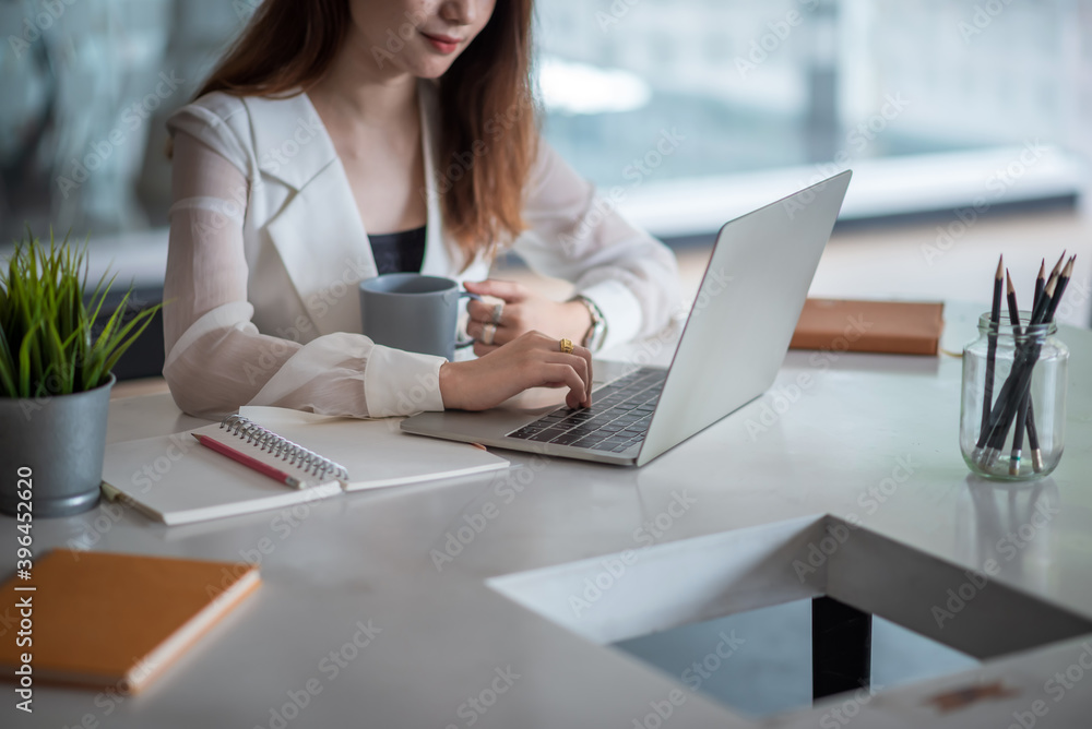 Businesswoman holding coffee cup and working with laptop computer in the office.