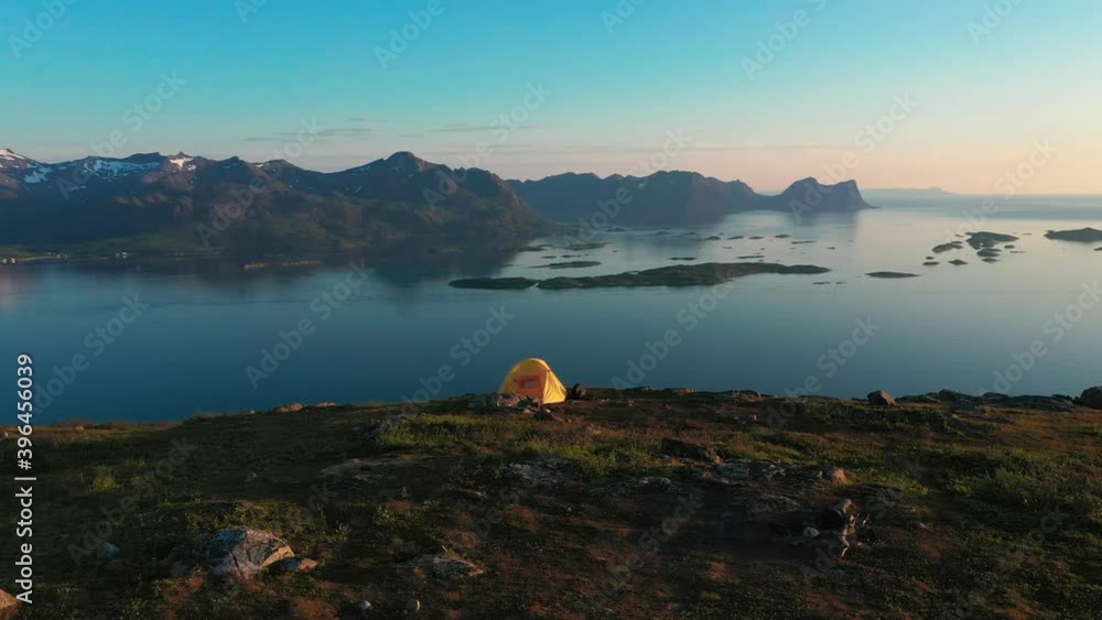 Aerial view around a tent high in the mountains of Senja, Norway, island and snowy peak background, during sunset - orbit, drone shot Aerial view around a tent high in the mountains of Senja, Norway, island and snowy peak background, during sunset - orbit, drone shot