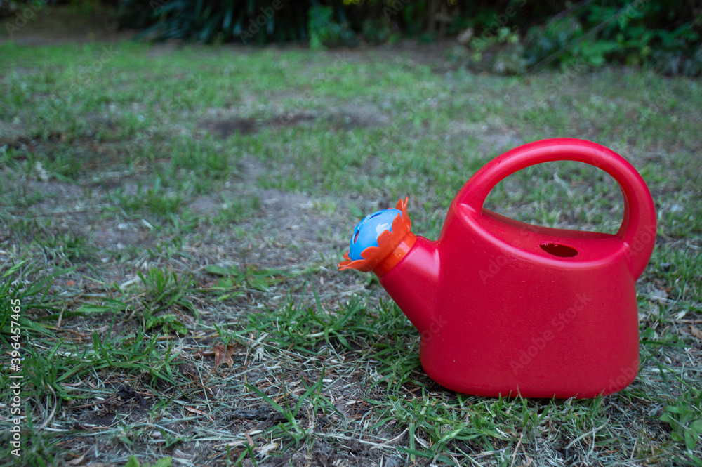 Red toy watering can in a garden