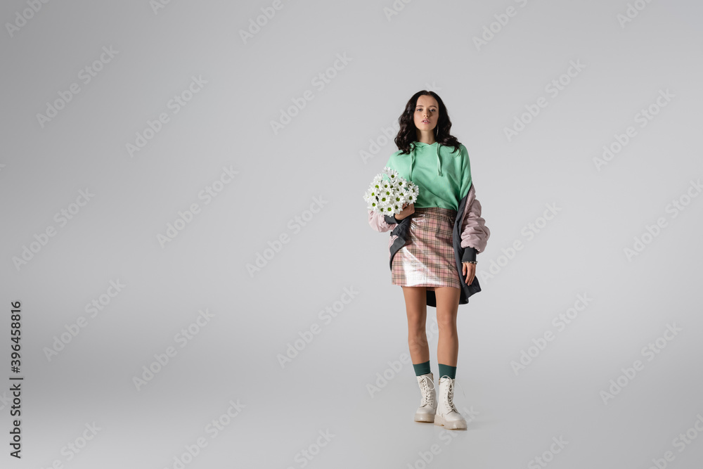 young woman in stylish winter outfit posing with flowers on grey background young woman in stylish winter outfit posing with flowers on grey background