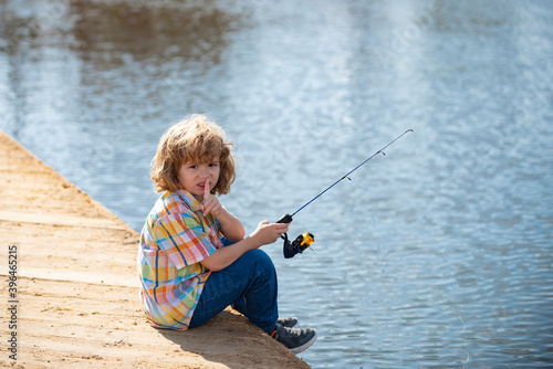 Serious, little boy child is fishing on the river with a fishing rod.
