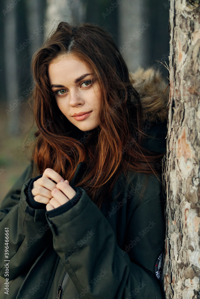 Fototapeta premium pretty red-haired woman in warm jacket near tree in nature forest