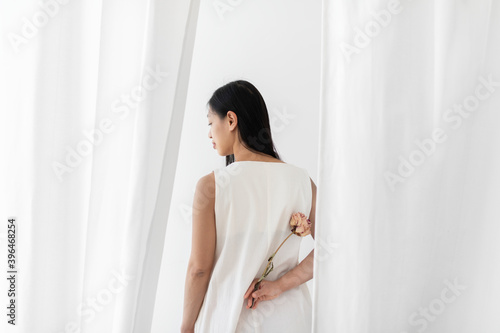 Asian woman with a dry pink peony flower in a hand among the white curtain