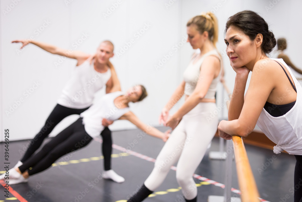 Obraz premium Group of people doing exercises using barre in gym with focus to kazakh woman in foreground in health and fitness concept