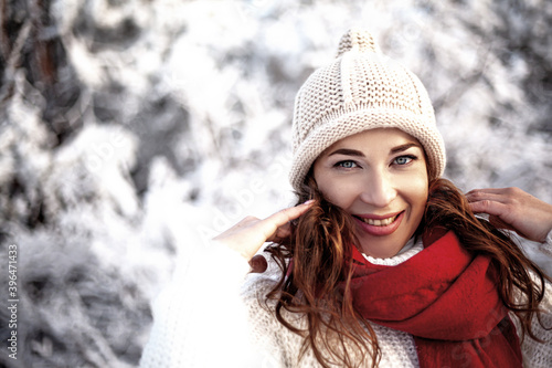 Happy f woman walking in the snowy winter day outdoor. Female mdel dressed white sweater and hat posing against the snow and sun