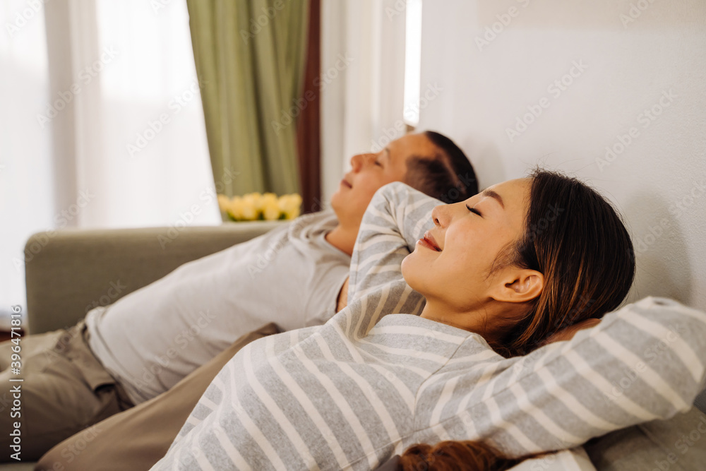 Side view of a couple relaxing on a sofa in living room at home. Caucasian and Asian woman breathing and resting while smiling and lying in couch indoors