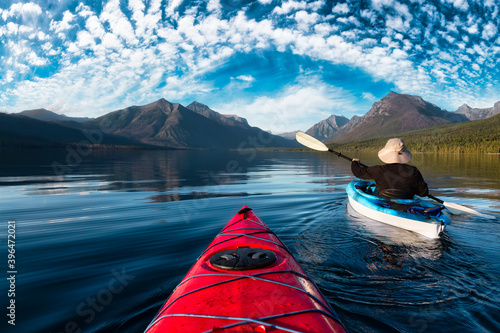 Adventurous Man Kayaking in Lake McDonald during a sunny summer evening with American Rocky Mountains in the background. Taken in Glacier National Park, Montana, USA. photo