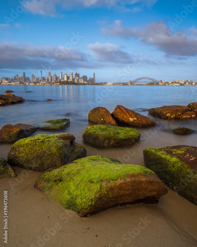 Sydney harbour during sunrise. City view with stones in foreground. Beautiful clouds in the blue sky.