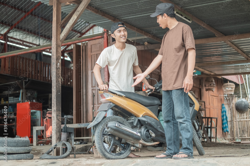male customer standing with hand gesture explains to the tire repairman that a motorbike tire has leaked at the tire repair shop male customer standing with hand gesture explains to the tire repairman that a motorbike tire has leaked at the tire repair shop