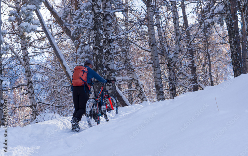 A man rolls a bicycle uphill in winter. Bicycle in the winter in the mountains. A man rolls a bicycle uphill in winter. Bicycle in the winter in the mountains.