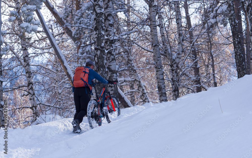 A man rolls a bicycle uphill in winter. Bicycle in the winter in the mountains.