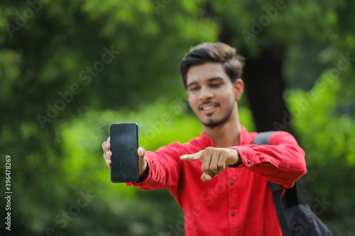 Young indian college student showing smart phone over nature background