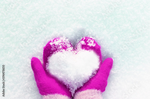 hands in knitted mittens with a heart made of snow on a winter day. ... Snowy heart in hands. Human hands in warm red mittens with a snowy heart on a background of snow. Love winter christmas or