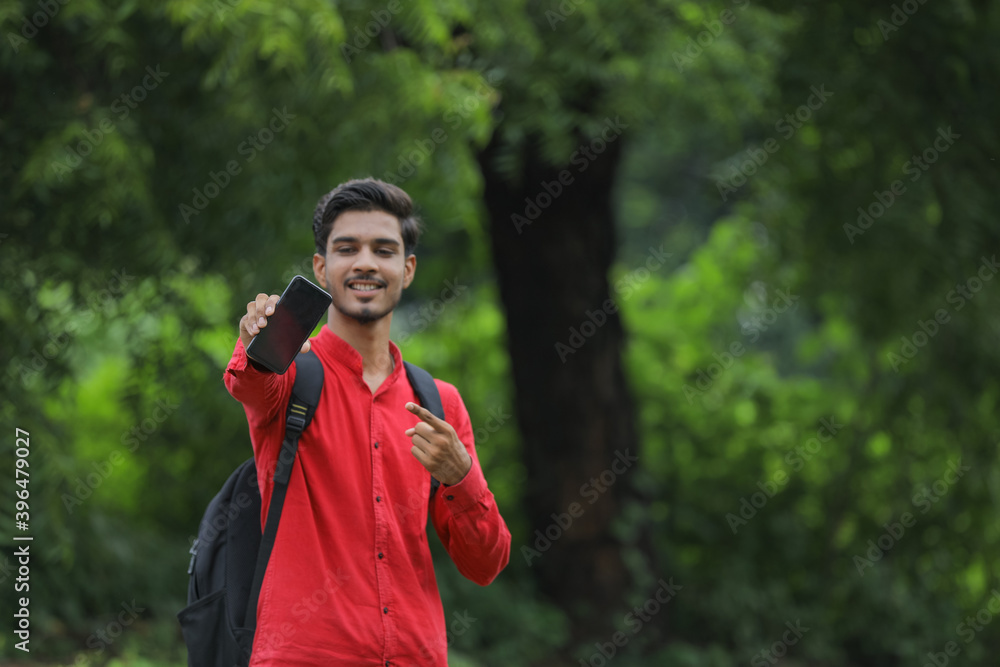 Young indian college student showing smart phone over nature background Young indian college student showing smart phone over nature background